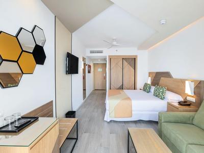 Modern hotel room with double bed, sofa, and hexagonal mirror wall decor.