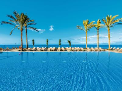 Large pool with palm trees and sea view under clear sky.