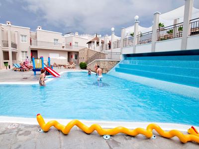 Niños jugando en la piscina azul de un hotel bajo un cielo nublado
