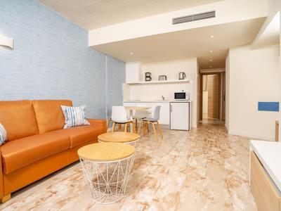 Modern eingerichtetes Wohnzimmer mit braunem Sofa, weißem Esstisch und offener Küche.