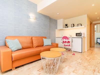 Helles Wohnzimmer mit orangefarbenem Sofa, zwei Tischen und Küchenzeile im Hintergrund.