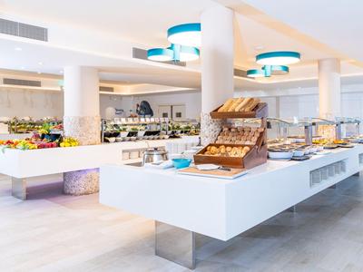 Helder verlichte buffetruimte met moderne witte tafels en diverse gerechten in een hotel.