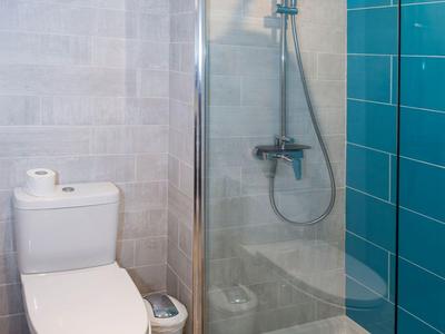 Heldere moderne hotel douche met glazen scheidingswand, blauwe tegels en wit toilet.