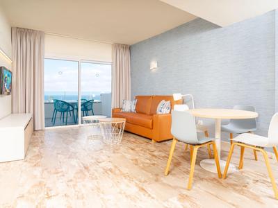 Modern eingerichtetes Wohnzimmer mit braunem Sofa, Esstisch und Balkon mit Meerblick.