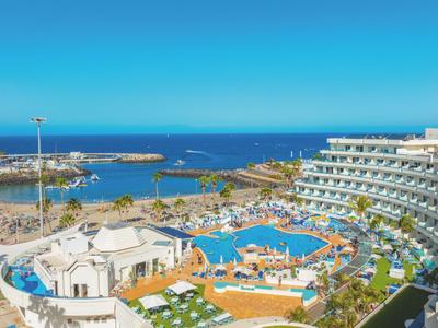 Moderner Hotelkomplex mit Pool, Liegestühlen und Meerblick unter klarem Himmel.