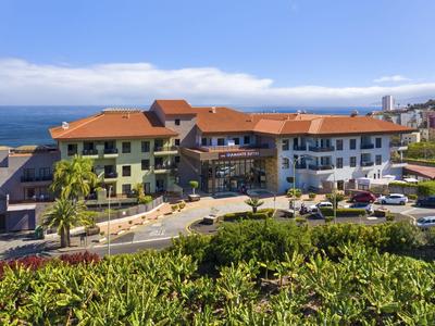 Hotel building with red roofs on the coast overlooking the sea under a clear sky.