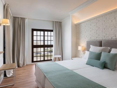 Nowoczesny pokój hotelowy z podwójnym łóżkiem, poduszkami i dużym oknem z zasłonami.