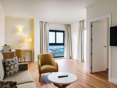 Nowoczesny pokój hotelowy z sofą, fotelem, okrągłym stolikiem i dużym oknem z widokiem.