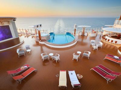 Vista de una terraza de hotel con piscina, tumbonas y mar al fondo al atardecer.