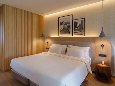 Habitación de hotel moderna con cama grande, paneles de madera y luz suave.