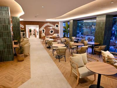 Café moderno con suelos de madera, sillones cómodos y grandes ventanales con vistas al exterior.