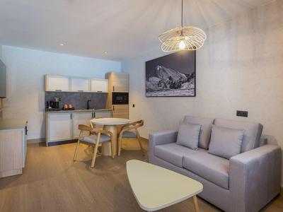 Área de estar moderna con sofá gris, mesa de comedor, cocina e iluminación contemporánea.