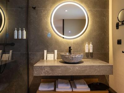 Bagno moderno con specchio rotondo illuminato, lavabo e asciugamani sotto il piano di lavoro.