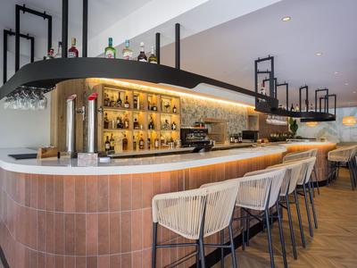 Área de bar moderna en hotel con taburetes cómodos y estantes iluminados llenos de botellas.