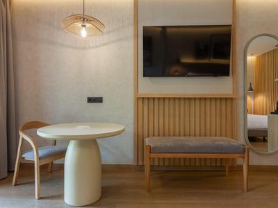 Moderne hotelkamer met kleine ronde tafel, stoel, bankje en wand-tv.
