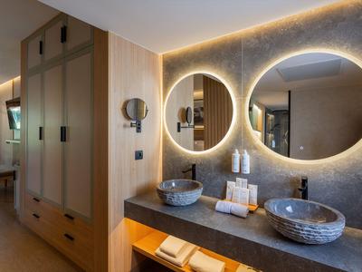 Moderne hotelbadkamer met verlichte ronde spiegels en stenen wastafels.