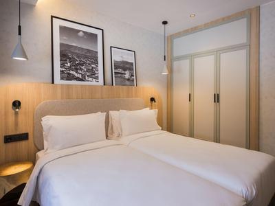 Knusse hotelkamer met tweepersoonsbed, nachtkastjes, lampen en ingelijste foto's aan de muur.