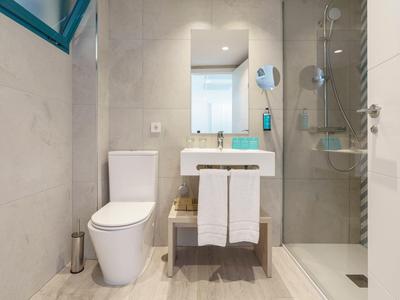 Moderní koupelna s WC, umyvadlem a skleněným sprchovým koutem, světlé stěny a podlaha.