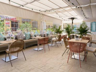 Cozy outdoor hotel terrace with wicker chairs, tables, and cushioned bench seating under a canopy.