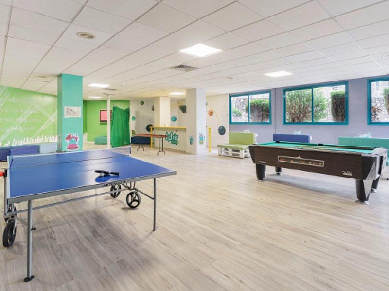 Bright game room with ping pong table, pool table, and large windows overlooking greenery.