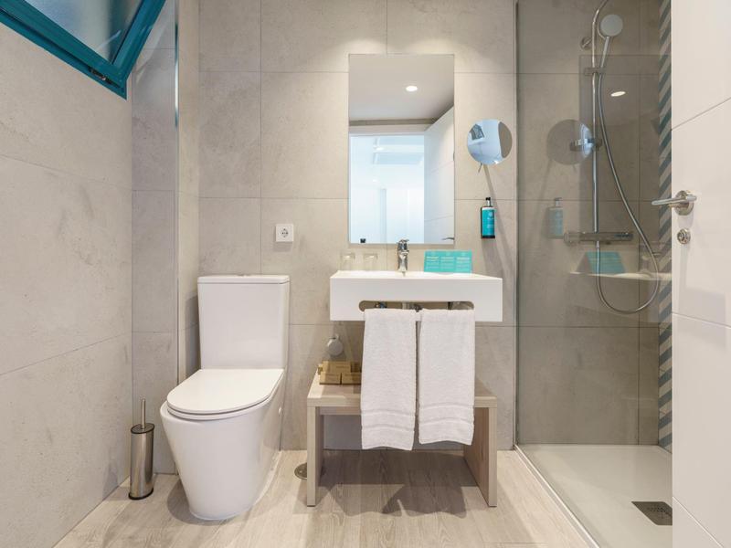 Salle de bain moderne avec WC, lavabo et douche vitrée, murs et sol clairs.