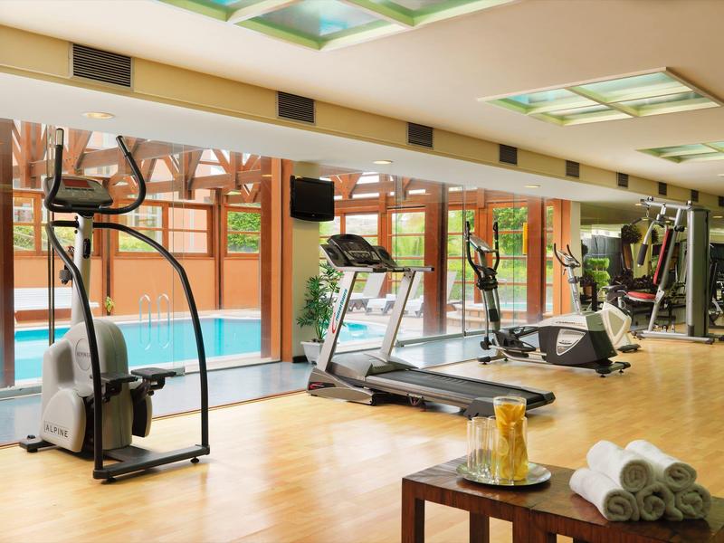 Palestra ben illuminata con tapis roulant e vista su una piscina all'aperto.