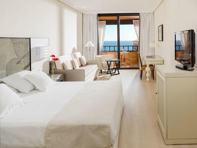 Helles, modernes Schlafzimmer mit Doppelbett, Sofa, großem Fenster und Blick auf eine Terrasse.