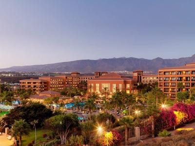 Resort extenso con varios edificios y áreas verdes al atardecer con montañas al fondo