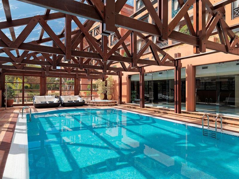 Piscina techada con vigas de madera y tumbonas en un hotel.