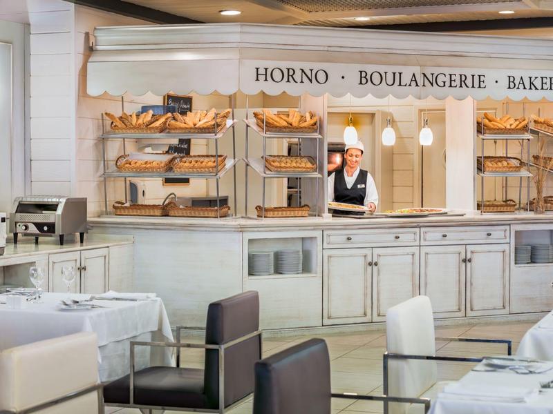 Panadería elegante con estantes de madera llenos de productos frescos y mesas puestas en el restaurante del hotel.