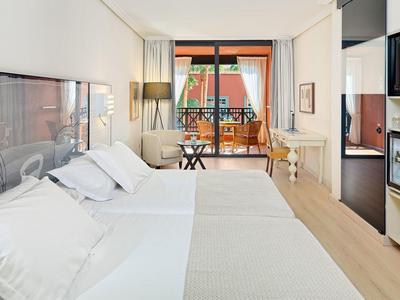 Bright hotel room with two single beds, balcony, and modern furnishings.