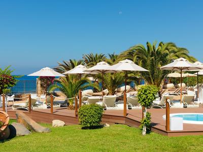 Pool area with umbrellas, lounge chairs, and sea view under clear sky.