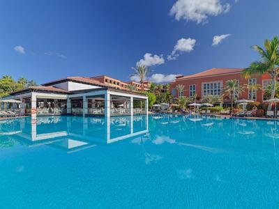 Large pool with palm trees and buildings under clear sky at a hotel resort.
