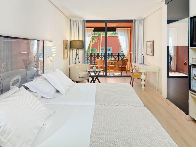 Bright hotel room with two beds, balcony seating, and modern decor.