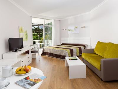 Lichte hotelkamer met bed, bank, tv en balkon met uitzicht.