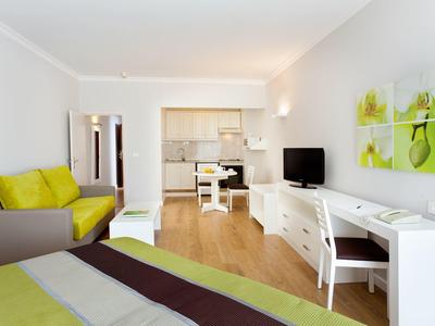 Lichte hotelkamer met bed, tv, bureau en comfortabele bank in groene en bruine tinten.