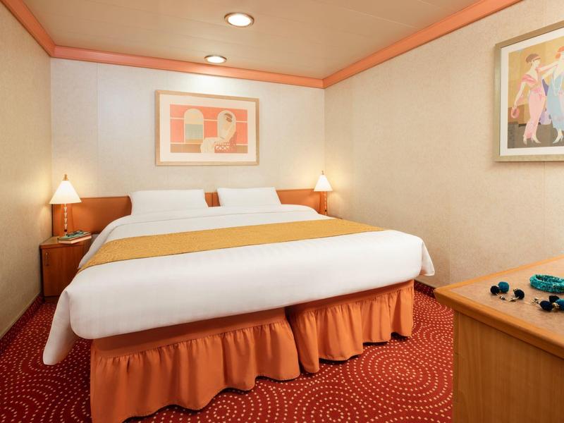 Habitación de hotel limpia con cama grande, alfombra roja y acabados en madera.