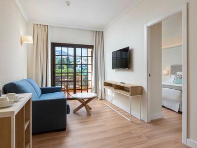 Sala de estar luminosa con sofá azul, TV montada y puerta con balcón en un hotel moderno.