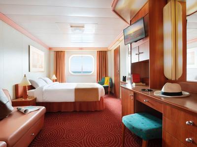 Lichte cruiseschipcabine met bed, rond raam en houten meubilair.