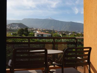 Balcony with chairs and table overlooking a valley with mountains in the background.