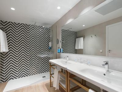 Modern hotel bathroom with double sink, large mirror, and chevron patterned shower curtain.