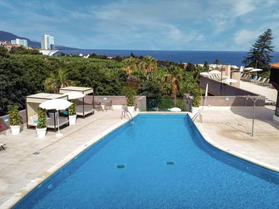 Outdoor pool area with loungers, umbrellas, and views of greenery and the sea.