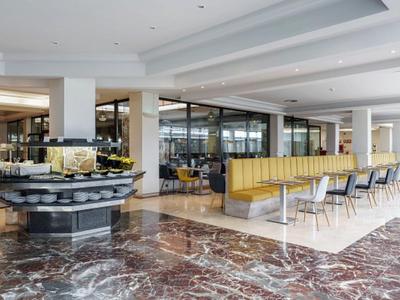 Moderne eetruimte in hotel met marmeren vloeren, buffetbalie en gele bankzitplaatsen.