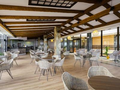 Bright breakfast room with wooden beams, rattan tables and chairs, and large windows.