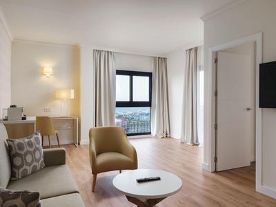 Soggiorno moderno con poltrona beige, divano, tavolo rotondo e grande finestra con vista sulla città.