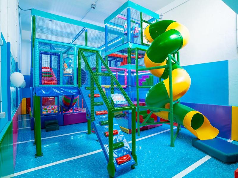 Bunter Indoor-Spielplatz mit Rutsche, Klettergerüst, weichem Boden und hellblauen Wänden.