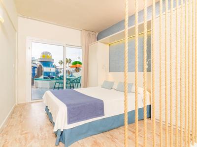Bright hotel room with double bed, wooden floor, balcony with chairs and sea view