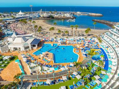 Großer Hotelpool mit Liegestühlen und Wasserrutschen, umgeben von Palmen und Meerblick.