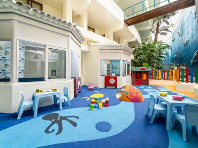 Aire de jeux intérieure lumineuse pour enfants avec petites tables, chaises et jouets colorés.