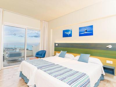 Habitación de hotel moderna con cama doble, decoración azul y vista al mar a través de grandes ventanales.